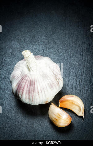 Tête d'ail et de girofle (Allium sativum) sur une surface en ardoise noire. Banque D'Images