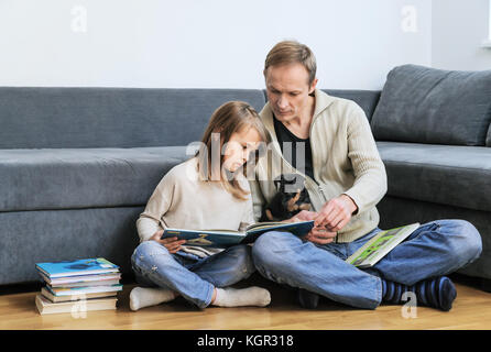 Père et fille sont la lecture de livres. le chiot est assis sur les jambes de l'homme. Banque D'Images