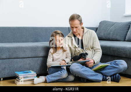 Père et fille sont la lecture de livres. le chiot est couché sur les jambes de l'homme. Banque D'Images