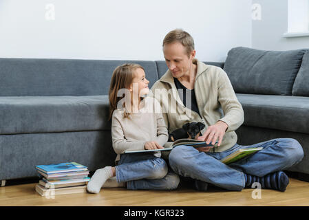 Père et fille sont la lecture de livres. le chiot est en train de dormir sur les jambes de l'homme. Banque D'Images