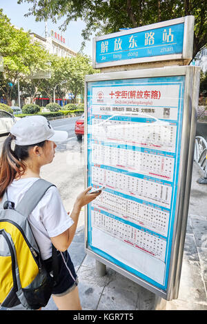 Guilin, Chine - 15 septembre 2017 : Chinese woman with backpack vérifie l'horaire à l'arrêt de bus au centre-ville de Guilin. Banque D'Images