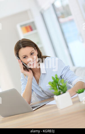 Woman in office talking on mobile phone Banque D'Images