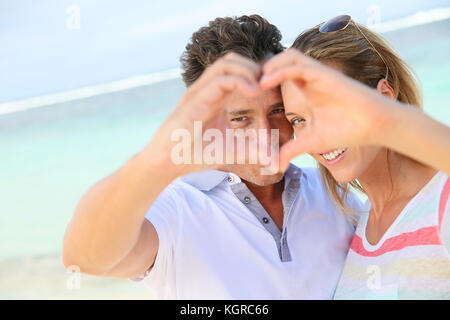 Couple romantique à la plage faire signe avec les mains du coeur Banque D'Images