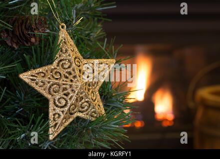 Étoile d'or accroché à un arbre de Noël avec une cheminée en arrière-plan Banque D'Images