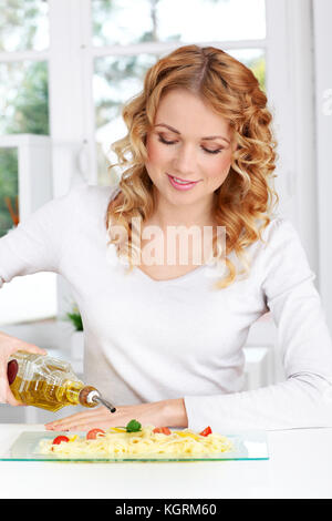 Blonde woman pouring olive oil sur plat de pâtes Banque D'Images