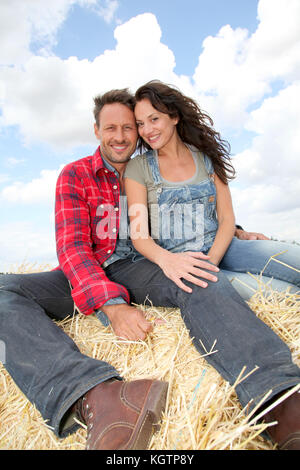 Heureux couple assis sur la balle dans les terres agricoles Banque D'Images