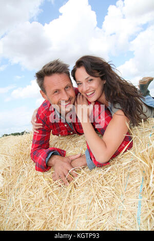 Heureux couple assis sur la balle dans les terres agricoles Banque D'Images