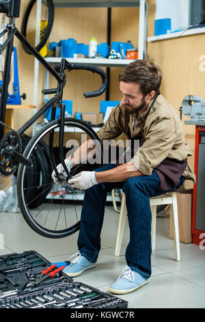 Jeune professionnel dans la réparation de vélo détail central de fixation de roue de bicyclette Banque D'Images