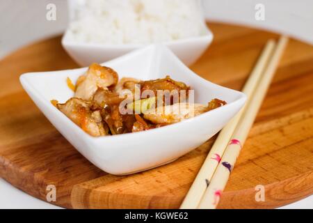 La cuisine chinoise servie dans de petits bols carré blanc sur planche de bois avec des baguettes en bambou Banque D'Images