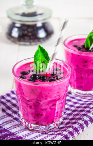 Les smoothies de cassis dans verre verres avec paille sur une table en bois blanc Banque D'Images