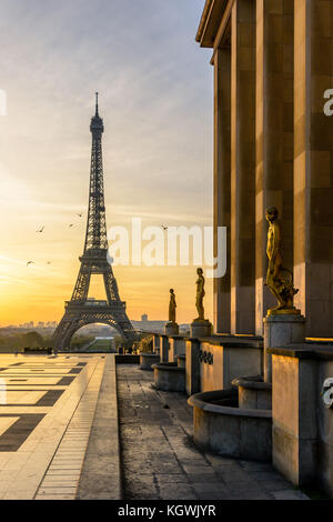 Le soleil levant éclaire l'esplanade du Trocadéro et ses statues en or alors que la Tour Eiffel se détache sur un ciel orange. Banque D'Images