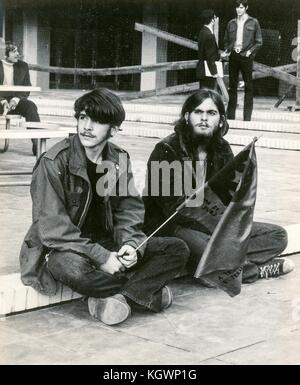 Deux étudiants masculins portant une tenue hippie sont assis sur une marche, l'un tenant un drapeau avec le visage du révolutionnaire Che Guevara, lors d'un sit-in étudiant anti-guerre du Vietnam à l'Université d'État de Caroline du Nord, Raleigh, Caroline du Nord, 1970. () Banque D'Images