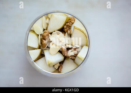 La bouillie de gruau aromatisé avec de la purée de banane, surmonté de tranches de poire, noix, amandes et miel, vue de dessus, servi dans une table ronde en verre clair, pl Banque D'Images