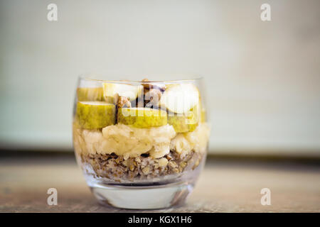 Petit-déjeuner gruau aromatisé avec de la purée de banane, surmonté de tranches de poire, noix, miel et amandes tranchées, vue d'un côté, servi dans un round gl Banque D'Images