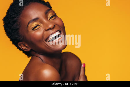 Close up of young African woman with makeup laughing contre fond jaune. Modèle féminin gaie aux couleurs de maquillage. Banque D'Images