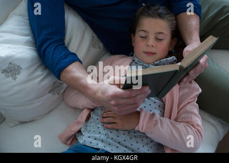 Girl sleeping while father reading book à côté d'elle dans la salle de séjour Banque D'Images