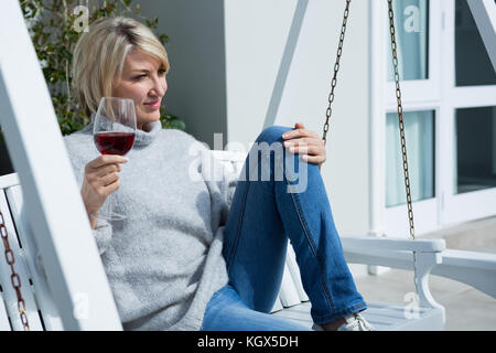 Femme sérieuse ayant du vin dans le porche d'une journée ensoleillée Banque D'Images