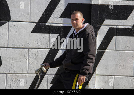 Un jeune homme, gopnik, assis sur un vélo à côté d'un mur recouvert de graffitis Banque D'Images