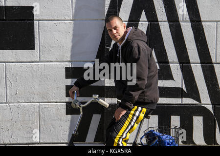 Un jeune homme, gopnik, assis sur un vélo à côté d'un mur recouvert de graffitis Banque D'Images