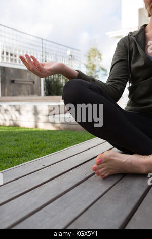 Mid section of woman practicing yoga in porche sur une journée ensoleillée Banque D'Images