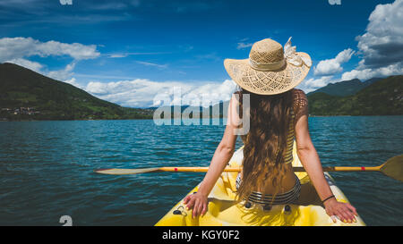 Jeune femme avec chapeau et de beaux cheveux longs en relaxant kayak sur lac alpin Banque D'Images