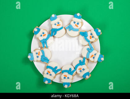 Le SNOWMAN sugar cookies décorés de marshmallow fondant, le glaçage royal bleu foulard et chapeau disposées en cercle sur une assiette de porcelaine. fond vert. Banque D'Images