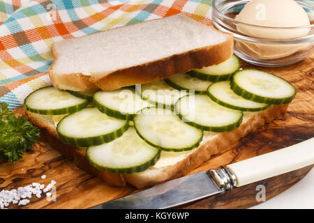 Préparer un blanc grillé sandwich avec concombre biologique sur une planche en bois Banque D'Images