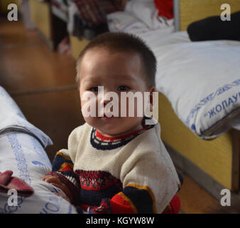 Petit garçon kazakh mignon avec asiatique avec des yeux cockeyés regardant quelqu'un avec la bouche ouverte portant un pull en laine d'hiver. Banque D'Images