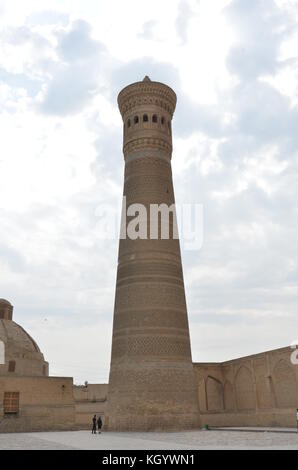 Grand minaret en pierre avec deux personnes à côté pour avoir une idée de l'échelle à Boukhara, Ouzbékistan. Banque D'Images