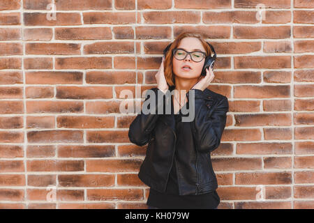 Portrait d'une jeune femme gaie blondhair profiter de la musique dans les écouteurs sur mur brique grunge background. Banque D'Images