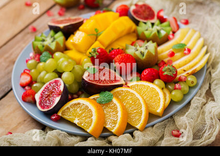 Plat de fruits et de baies. la mangue, kiwi, fraises, raisins, figues, poire et orange.. une cuisine végétalienne menu diététique. Banque D'Images