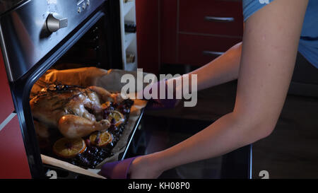 Sortir les mains des femmes de poulet rôti entier sur la plaque du four chaud. Banque D'Images