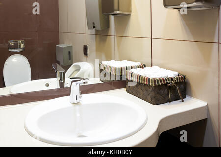 Un gros plan d'un lavabo blanc moderne, à côté il y a une boîte avec des serviettes de nettoyage, sèche-mains automatiques, dans l'arrière-plan de toilettes dans les toilettes Banque D'Images