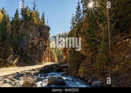 Scenic autumn vue depuis le chemin de terre à travers la porte dans le rouge, montagnes, rivière, arbres et le soleil contre un ciel bleu sur une journée ensoleillée Banque D'Images