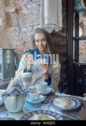 Une charmante jeune fille aux cheveux noirs se repose dans un café confortable. Le café est sur sa table. La jeune fille aime le goût de la crème glacée. Banque D'Images