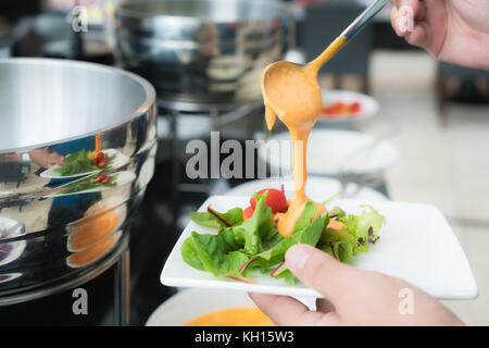 Cuillère à soupe crémeuse de Thousand Island Dressing étant versé sur de la salade du jardin frais dans le petit-déjeuner buffet à l'hôtel. Banque D'Images