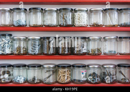 Divers composants matériels stockés dans des pots de confiture en verre sur trois étagères dans un atelier d'accueil Banque D'Images