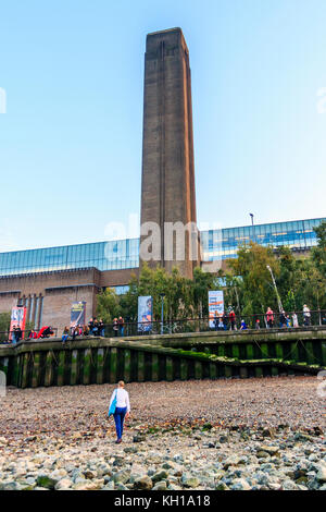 Une femme marche sur la Tamise estran à marée basse à Bankside, Londres, Royaume-Uni, les soirée d'automne, la Tate Modern de l'arrière-plan Banque D'Images