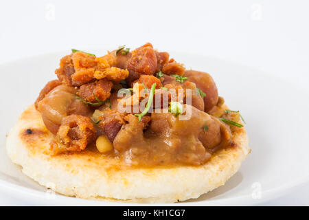 Arepa colombienne traditionnelle surmontée d'haricots et de couenne de porc Banque D'Images