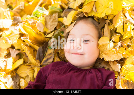 Happy little girl en jaune vif pile de feuilles ratissées Banque D'Images