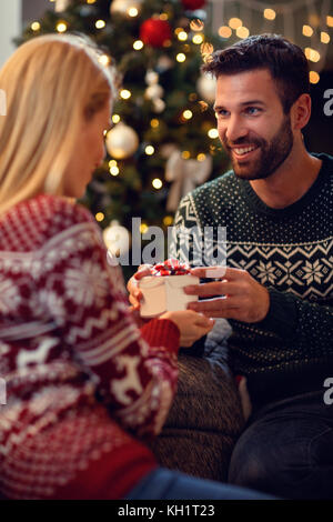 Smiling man presenting cadeau de Noël à happy young woman at home Banque D'Images