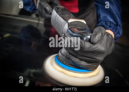 Close-up of a mechanic avec un prisme bleu et des gants protecteurs clignote le black metal machine bouclier de petites rayures après peinture Banque D'Images