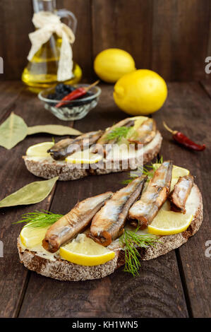 Sandwich avec le poisson fumé le capelan (anchois), citron sur le pain de seigle noir. snack sur une table en bois sombre. Banque D'Images