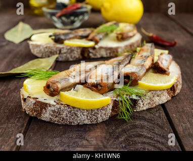 Sandwich avec le poisson fumé le capelan (anchois), citron sur le pain de seigle noir. snack sur une table en bois sombre. Banque D'Images