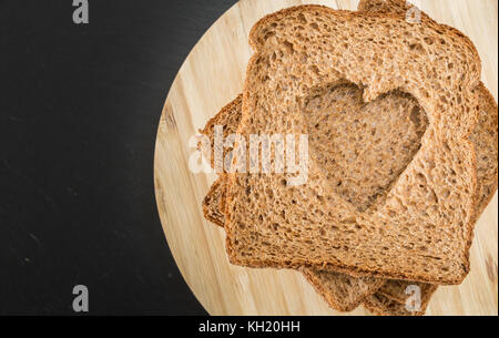 Tranches de pain de grains entiers en forme de cœur, sur la plaque en bois Banque D'Images