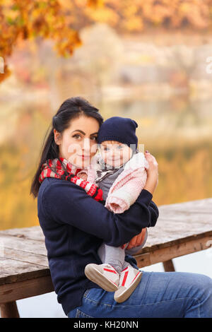 Portrait de jeune mère avec ma petite fille à l'automne forêt près de la rivière. maman holding baby girl à mains. famille heureuse, l'amour parental, la mer d'automne Banque D'Images