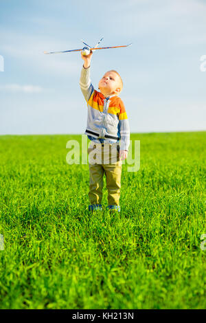 Happy kid Playing with toy airplane against blue sky background d'été. boy mousse jet avion dans champ vert. meilleur concept de la petite enfance. Banque D'Images