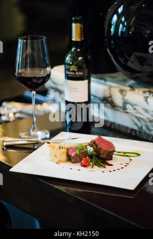 Un plat de chop d'agneau accompagné d'une bouteille et d'un verre de vin rouge sur une table noire Banque D'Images