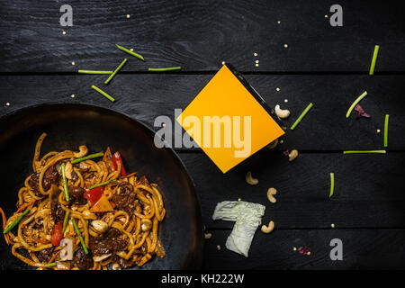 Udon nouilles sautés avec de la viande et les légumes dans le wok casserole sur fond de bois noir. avec un fort pour les nouilles vue d'en haut. Banque D'Images