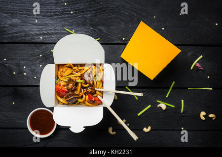 Udon nouilles sautés avec de la viande et des légumes dans une boîte sur fond noir. avec des baguettes et de la sauce. vue d'en haut. Banque D'Images